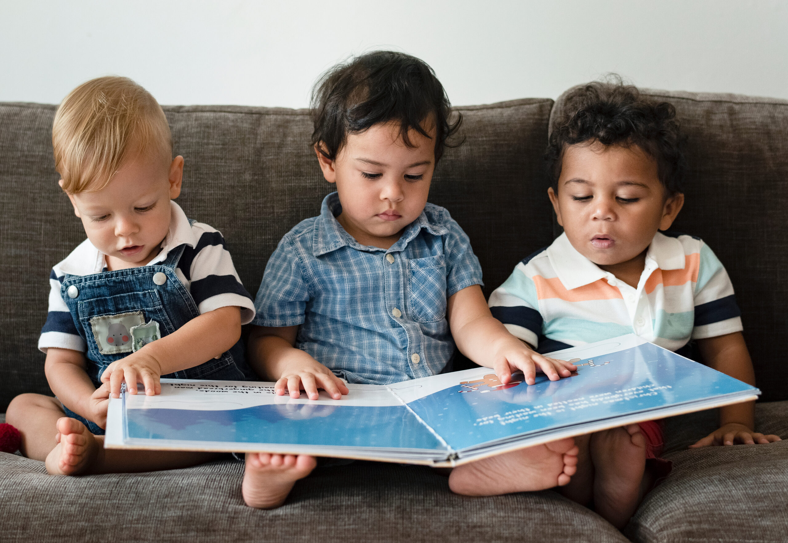 3 young boys are ready a book, showing early literacy.