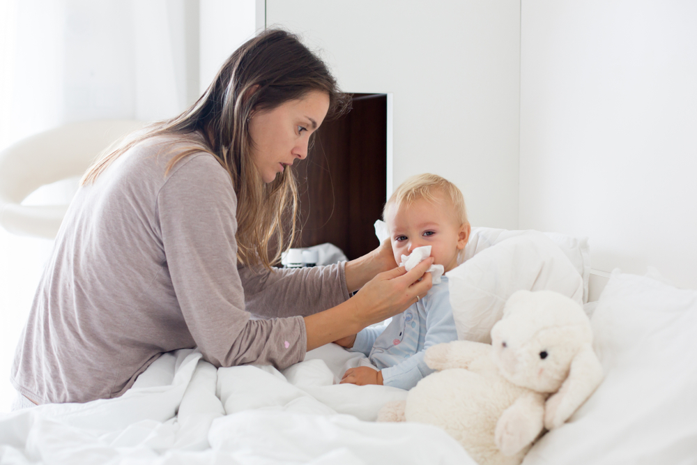 Baby suffering from common childhood illness, mom wiping baby's nose.